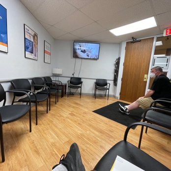 Patient sitting in a small clinic waiting room watching TV.
