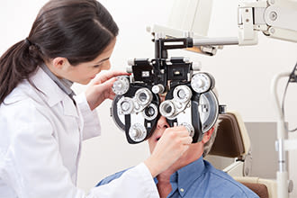 Optometrist adjusting a phoropter while examining a patient’s vision.
