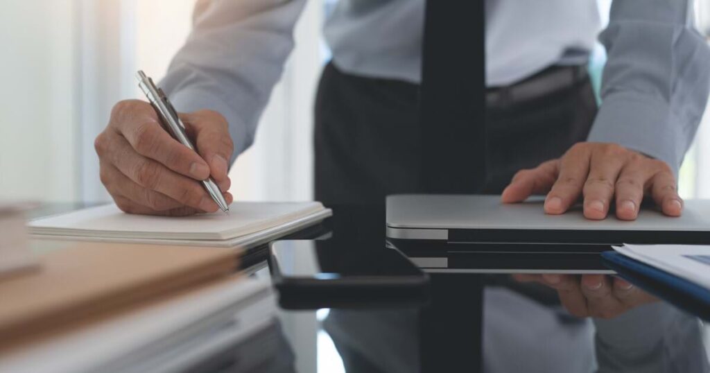 A professional writes notes on a pad while resting a hand on a closed laptop.
